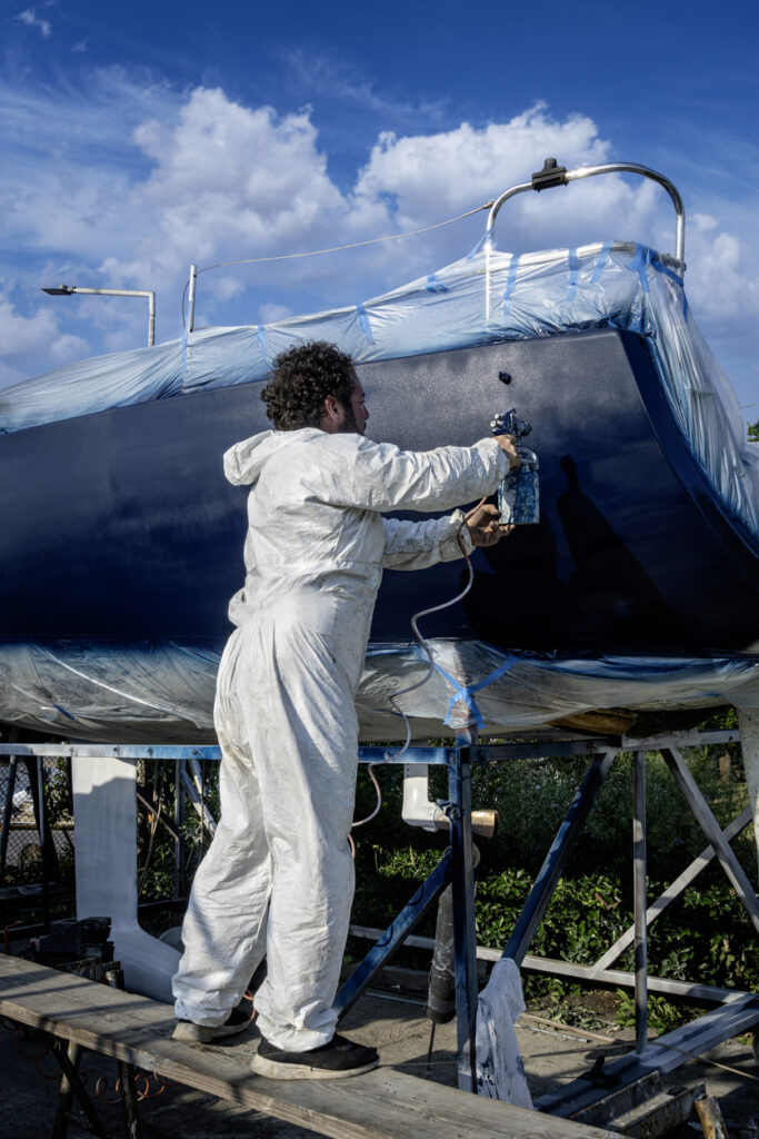 Worker spray painting the hull of a sailing yacht