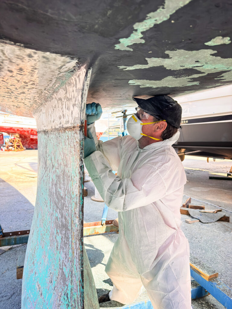 Technician scraping antifouling from a yacht hull ashore